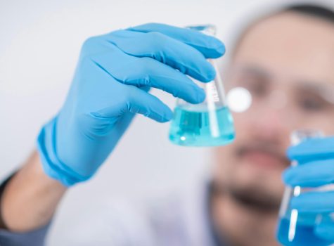 Laboratory scientist examining blue liquid in flask, wearing protective equipment