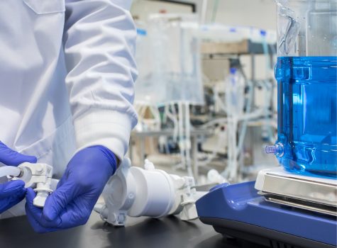 Lab technician in cleanroom gloves making an aseptic connection on a Mixed4Sure single-use bottle mixing system with fluid-filled container