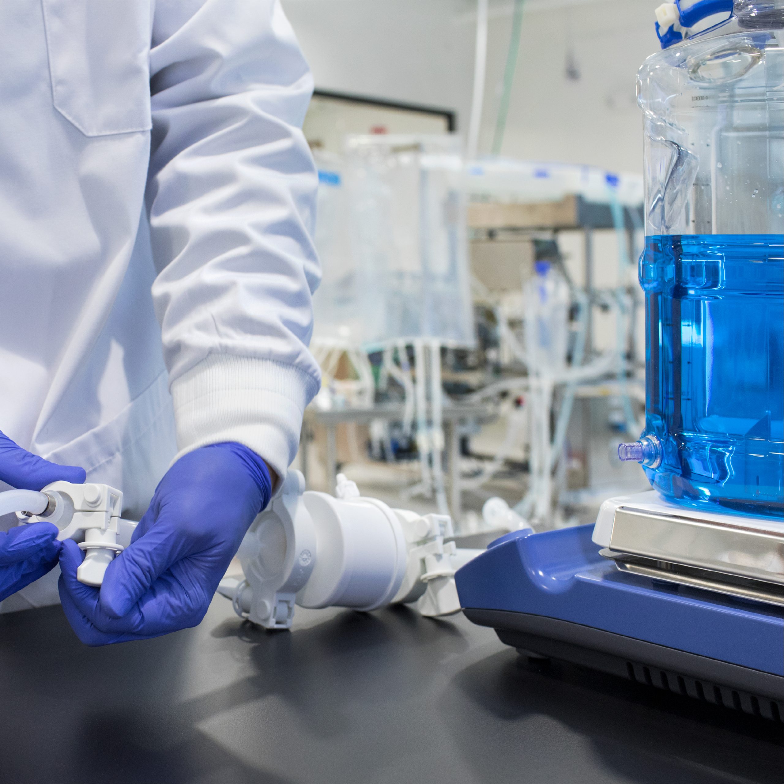Lab technician in cleanroom gloves making an aseptic connection on a Mixed4Sure single-use bottle mixing system with fluid-filled container