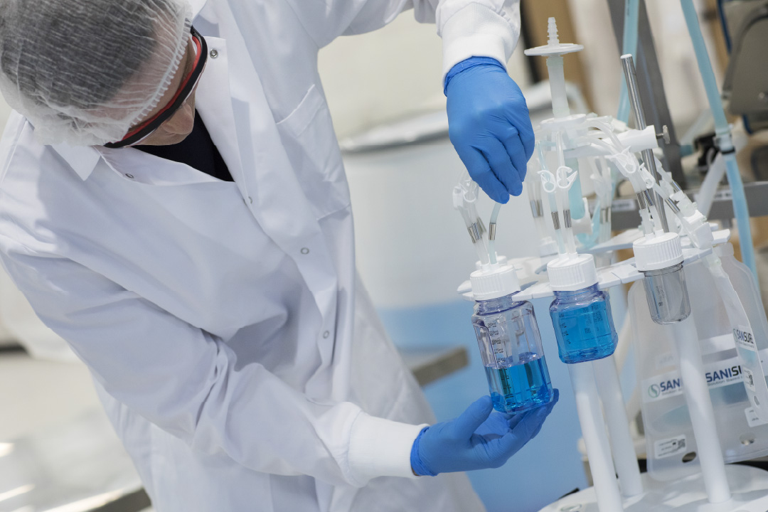 SaniSure one2sample single-use bag filled with blue process fluid, suspended from a stand with a three-line tubing assembly in a laboratory setting